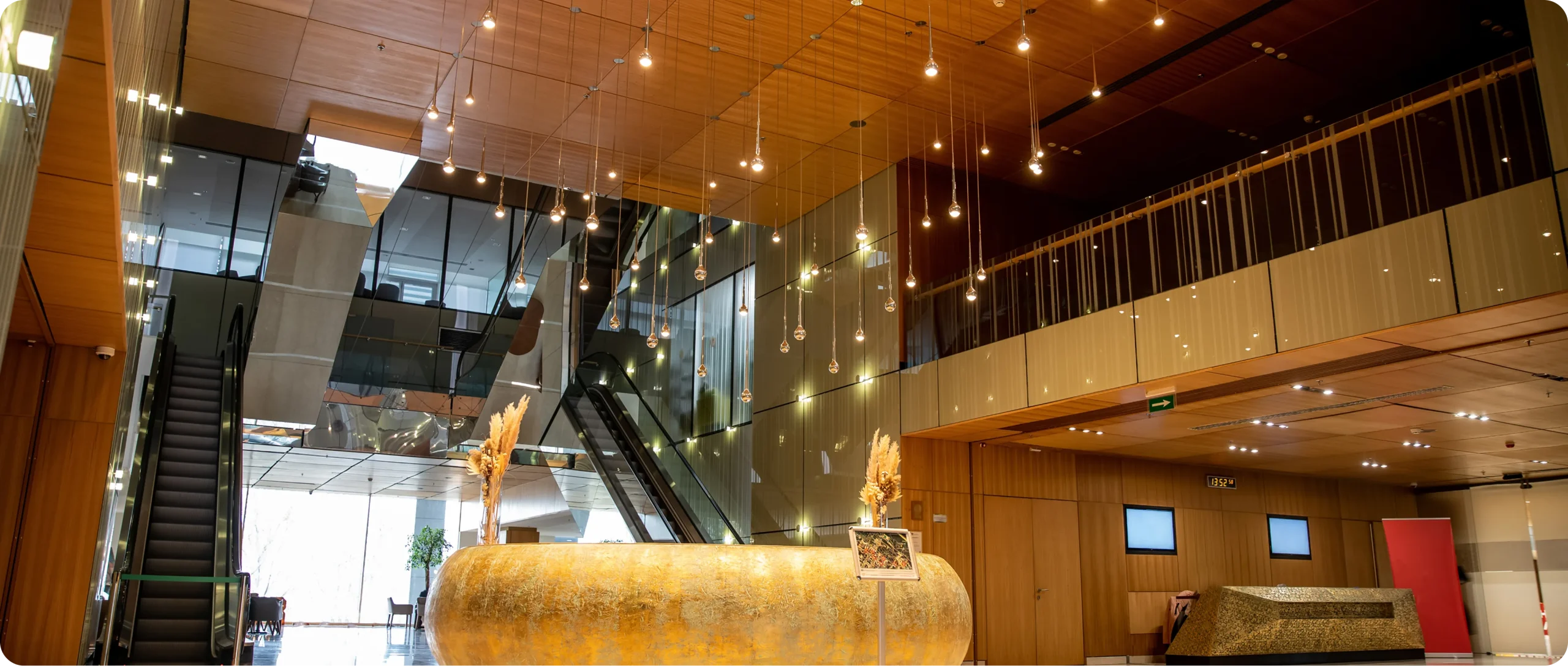 Grand timber-panelled foyer with escalators, pendant lights and a gold reception desk