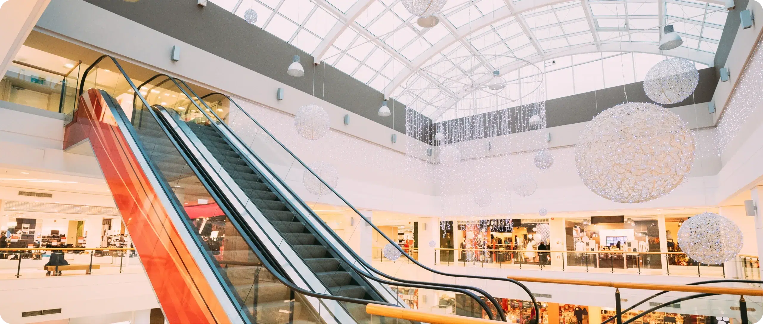 Hygienic and well-kept shopping centre Shopping centre interior with escalators, storefronts and a glass atrium roof