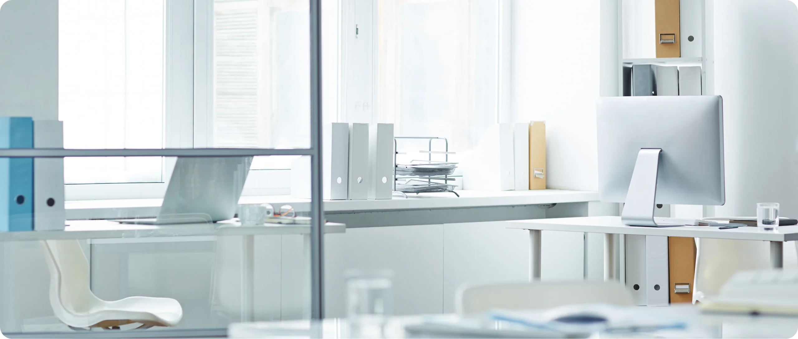 Bright white office with desks, a computer monitor and lever-arch folders on the windowsill