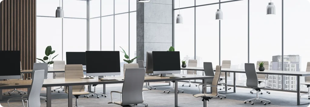 Modern open-plan office with rows of desks, monitors and floor-to-ceiling city views